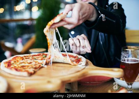 Une femme prend une tranche de pizza dans une pizzeria. Fromage tirant, pizza délicieuse. Vue avant. Banque D'Images