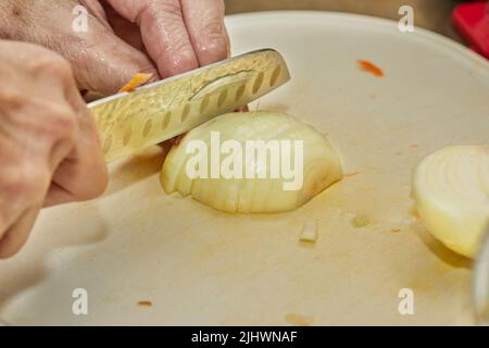 Le chef coupe l'oignon en tranches sur le tableau dans la cuisine maison. Banque D'Images