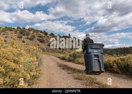 Un homme roule une grande poubelle noire sur une route de gravier dans la campagne du Nouveau-Mexique, aux États-Unis. Banque D'Images