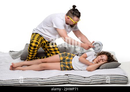 Famille portrait pleine longueur en pyjama à carreaux jaune sur mur blanc de studio. Le père se réveille en dormant la petite fille à poil court. Daddy pointant Banque D'Images