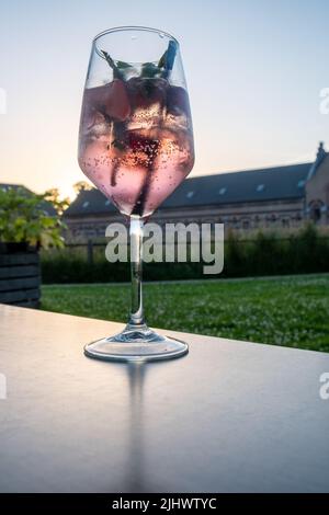 Cocktail rose, cocktail de mocktail ou autre boisson alcoolisée sur la table près des bâtiments historiques du parc et nuage de coucher de soleil dans un cadre rural. Photo de haute qualité Banque D'Images