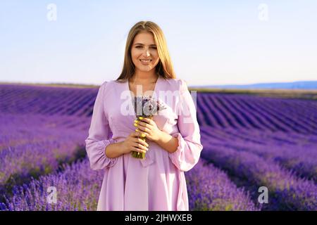 Jeune femme en robe tenant un bouquet de fleurs debout dans le champ de lavande Banque D'Images