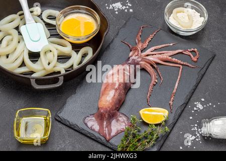 Calmar sur panneau de pierre. Calamars coupés en anneaux dans la poêle. Battez les œufs crus, le beurre et la farine dans des bols sur la table. Vue de dessus. Arrière-plan noir Banque D'Images