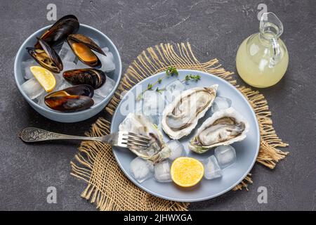 Huîtres, glace, citron et fourchette sur l'assiette. Palourdes dans les coquilles dans le bol. Bouteille de jus de citron. Pose à plat. Arrière-plan noir Banque D'Images