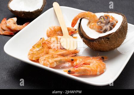 Soupe de crème de fruits de mer à la noix de coco, crevettes et cuillère en bois sur une assiette blanche. Vue de dessus. Arrière-plan noir Banque D'Images