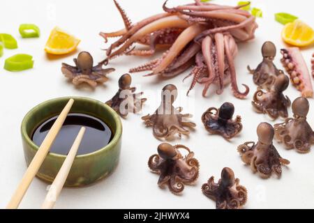 Sauce soja dans un bol et bâtonnets de bambou. Poulpes bouillis et calmars avec tentacules sur la table. Vue de dessus. Arrière-plan blanc Banque D'Images