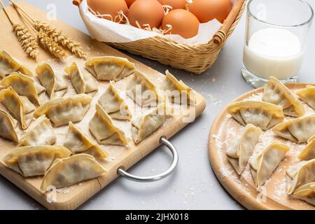 Boulettes de gyoza brutes sur une planche à découper. Œufs dans un panier en osier et un verre de lait. Vue de dessus. Arrière-plan gris. Banque D'Images