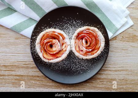 Assiette de mini-tartes aux pommes en forme de rose savoureuses et saines arrosées de sucre glace Banque D'Images