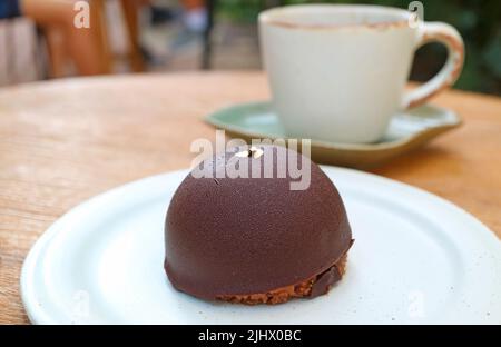 Gros plan sur les gâteaux Dome à la mousse au chocolat avec une tasse de café floue en toile de fond Banque D'Images