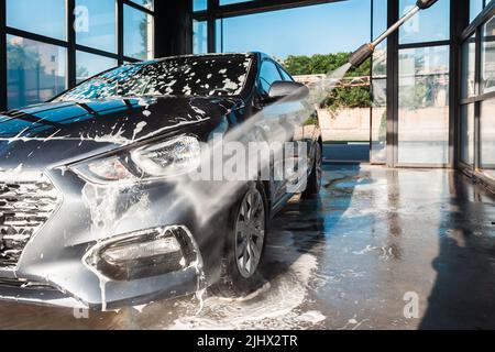 Lavage de voiture en libre-service. Un homme lave la mousse de sa voiture avec de l'eau d'un tuyau sous pression à un lavage de voiture en libre-service. Banque D'Images