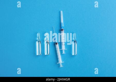 Flacons en verre médical et seringues d'injection isolés sur fond bleu, vue de dessus. Santé, vaccination, concept de pandémie. Banque D'Images