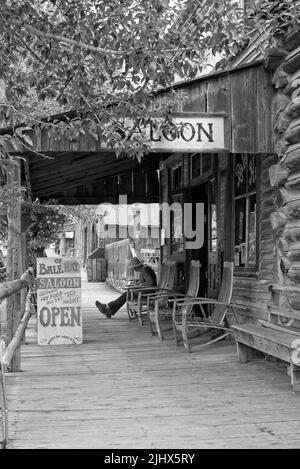 Échelle de gris verticale d'un homme assis sur une chaise à l'avant du Saloon Banque D'Images