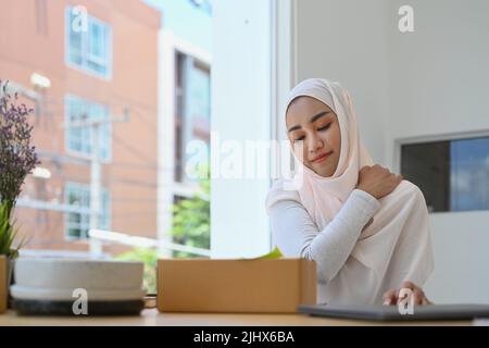 Femme d'affaires musulmane surtravaillée massant le cou dur frottant les muscles tendus, souffrant de douleurs au cou Banque D'Images