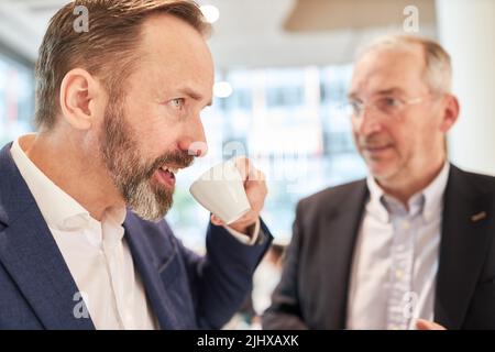 Homme d'affaires buvant une tasse d'espresso lors d'une pause avec des partenaires d'affaires en arrière-plan Banque D'Images