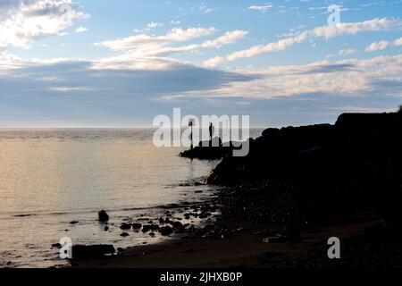 silhouette d'un homme pêche en mer du point sur les rochers au crépuscule Banque D'Images