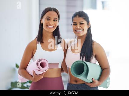 Rejoindre ces cours a été la meilleure décision jamais prise. Portrait de deux jeunes femmes sportives tenant des tapis d'exercice dans un studio de yoga. Banque D'Images