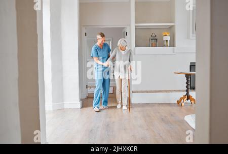 Vous vous renforceront de jour en jour. Une infirmière aide une femme âgée avec un bâton de marche dans une maison de retraite. Banque D'Images