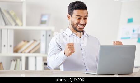 Jeune homme d'affaires de course mixte heureux et excités qui se réjouit de son soutien tout en travaillant seul sur un ordinateur portable dans un bureau au travail. Un patron mâle hispanique Banque D'Images