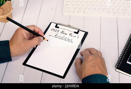 Les mains écrivant une liste des résolutions du nouvel an 2023 sur un tableau à pince sur un bureau en bois. Banque D'Images