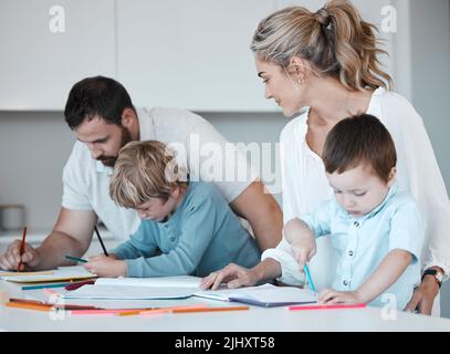 Jeune famille caucasienne assise à la maison. Parents aimant aidant leurs petits enfants à faire leurs devoirs. Des frères et sœurs insouciants se sont concentrés pendant l'écriture Banque D'Images