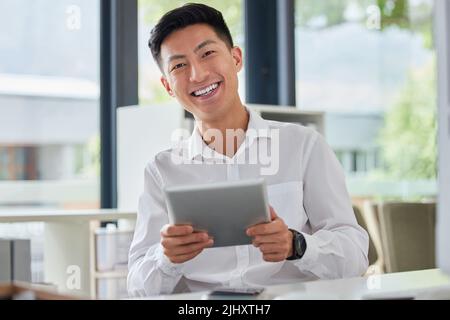 Jeune homme d'affaires asiatique heureux utilisant les médias sociaux sur une tablette numérique au bureau. Un chinois souriant vérifiant un e-mail sur un Banque D'Images