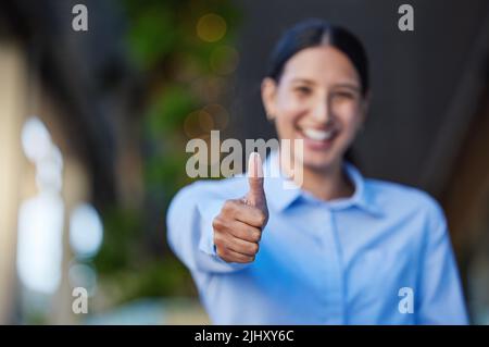 Gros plan d'une course mixte gaie femme d'affaires souriante faisant des pouces vers le haut geste à l'extérieur. Jeune femme hispanique montrant un bon symbole Banque D'Images