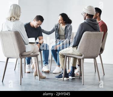 Homme ayant une panne pendant la séance de thérapie de groupe au sujet de la dépendance. Ami qui soutient l'homme de race mixte en pleurs dépressifs au groupe psychologique Banque D'Images