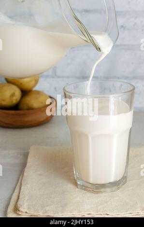 Le lait de pomme de terre est versé dans un verre à partir d'un pot en verre. Une nouvelle tendance à manger sainement. Concept de nourriture alternative. Lait de légumes pour les végétaliens. Orientation verticale Banque D'Images