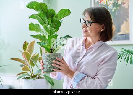 Femme d'âge moyen souriante avec plante en pot à la maison Banque D'Images