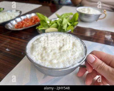 Babeurre, boisson traditionnelle au yaourt ou boisson connue sous le nom d'ayran en turc avec mousse dans la tasse en métal argenté sur la table en dinde. Babeurre, traditionnel Banque D'Images