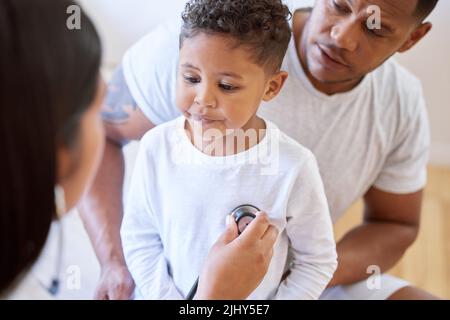 Enfant malade au bureau des médecins avec sa mère. Petit garçon assis avec son père tandis qu'une pédiatre prend une écoute avec un stéthoscope à Banque D'Images