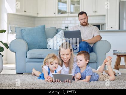 Mère et deux enfants regardant quelque chose sur une tablette numérique. Petite fille et petit garçon regardant des vidéos de dessin animé éducatives ou sur appel vidéo avec une tablette. Papa Banque D'Images