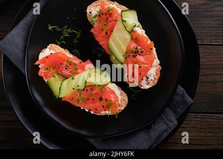 Sandwichs. Toast au saumon avec fromage à la crème, concombre, sésame noir et microverts sur fond de table en bois. Fruits de mer. Une alimentation saine. Photographie Banque D'Images