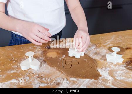 Une petite fille fabrique des biscuits en forme de cœur à partir de pâte de seigle. Le concept de la Saint-Valentin et de la cuisson saine. Cuisson des biscuits en gros plan. Banque D'Images