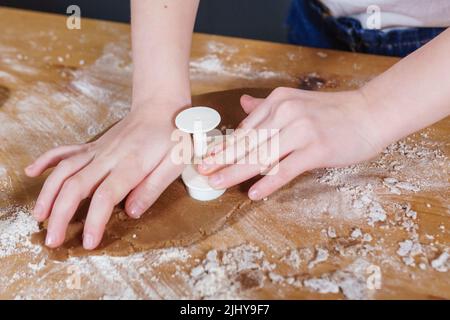 Une petite fille fabrique des biscuits en forme de cœur à partir de pâte de seigle. Le concept de la Saint-Valentin et de la cuisson saine. Cuisson des biscuits en gros plan. Banque D'Images