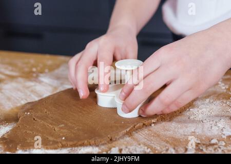 Une petite fille fabrique des biscuits en forme de cœur à partir de pâte de seigle. Le concept de la Saint-Valentin et de la cuisson saine. Cuisson des biscuits en gros plan. Banque D'Images