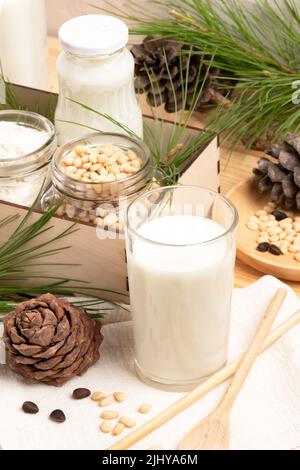 Lait de cèdre en verre et en bouteille, ingrédients noix et farine en pots en boîte, cônes, branches, cuillère. Lait non laitier de remplacement. Lait biologique sain RE Banque D'Images