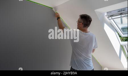 Le peintre enlève le ruban de masquage et crée une bordure nette entre une partie peinte en gris et en blanc d'un mur. Banque D'Images