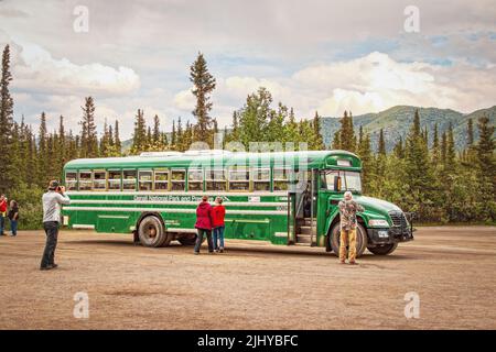 06-22-2002 Denali Alaska USA - Green transit bus dans le parc national Denali avec des touristes - un prenant une photo - et arbres et montagnes à feuilles persistantes en b Banque D'Images