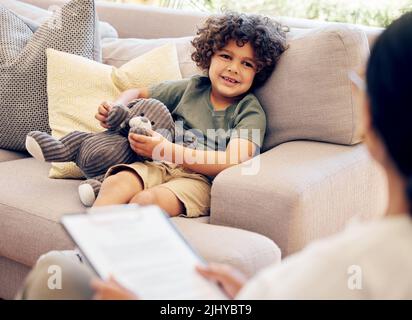 Aimez-vous votre nouvelle maison. Un petit garçon assis avec son teddybear lors d'une consultation avec un physiothérapeute. Banque D'Images