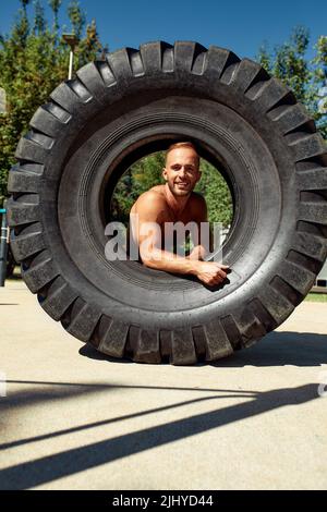 Homme fort entraînement entraînement levage grand pneu en plein air gym. Sportif jeune adulte caucasien gars de bascule grande roue sur la nature. Équipement fait main sport Banque D'Images