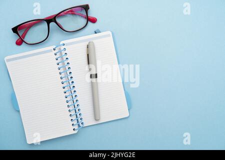 Vue de dessus d'un bloc-notes, de lunettes et d'un stylo isolés sur une table blanche Banque D'Images