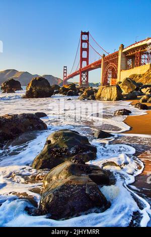 Les vagues se écrasont autour de rochers sur la plage à côté du Golden Gate Bridge à San Francisco, près du coucher du soleil Banque D'Images