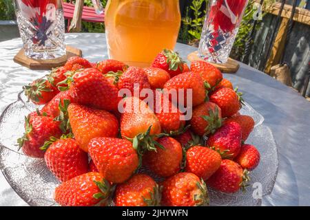 Plat en verre rempli de fraises fraîches avec jus et verres à l'arrière Banque D'Images