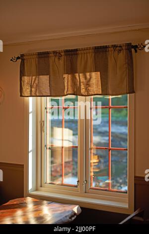 Grande fenêtre de cuisine avec lumière du soleil sur une table en bois. Maison rustique avec une vue extérieure qui illumine la chambre en été. Coin confortable dans Banque D'Images