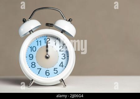 Douze heures sur l'alarme. Un réveil blanc se trouve sur une table blanche. La main de l'horloge pointe à 12 heures. Il est temps de passer à l'heure d'été ou d'hiver Banque D'Images