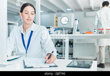Établir des faits fiables. Un jeune scientifique écrit des notes tout en travaillant sur un ordinateur dans un laboratoire. Banque D'Images