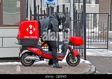 Jeune inconnu Nova Poshta Courier en costume noir sur moto livre les articles dans un grand contenant rouge. Banque D'Images