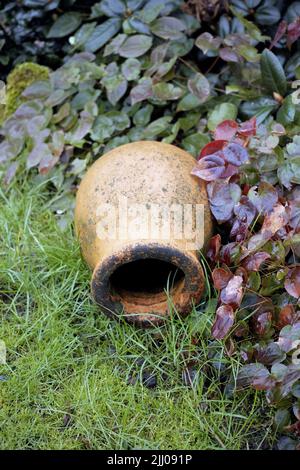 Un pot en céramique simple, ancien, vintage et décoratif, allongé sur une longue herbe verte non coupée dans un jardin intérieur à l'extérieur. Décoration extérieure rustique, négligée Banque D'Images