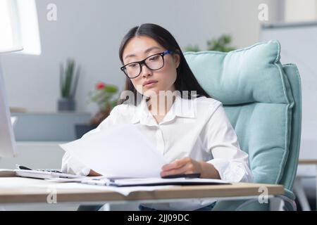 Travailler avec des documents. Portrait d'une jeune belle femme d'affaires asiatique comptable travaille avec des documents et des rapports. Assis au bureau, écrire. Banque D'Images